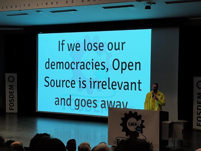 Photo from the FOSDEM 2026 showing a slide with the text: "If we lose our democracies, Open Source is irrelevant and goes away."